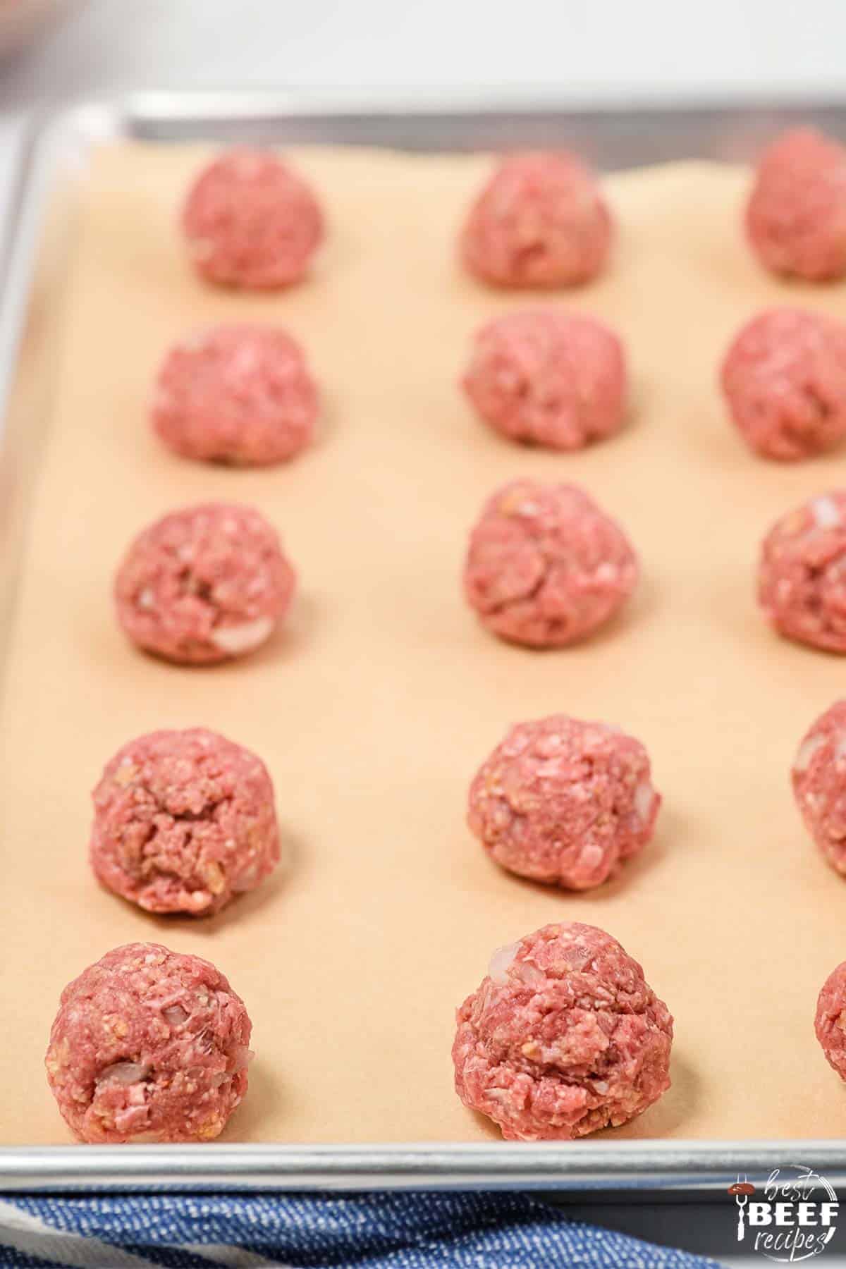 Meatballs rolled and lined on parchment paper on a baking sheet