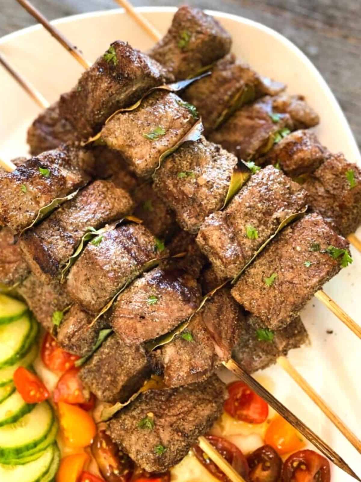 Grilled beef kabobs on a white plate with veggies