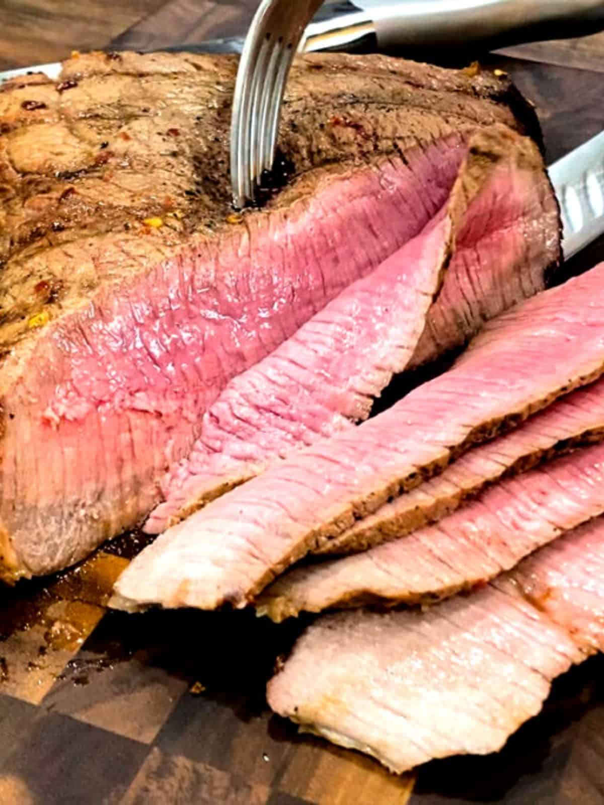Grilled London Broil being sliced on a wood cutting board