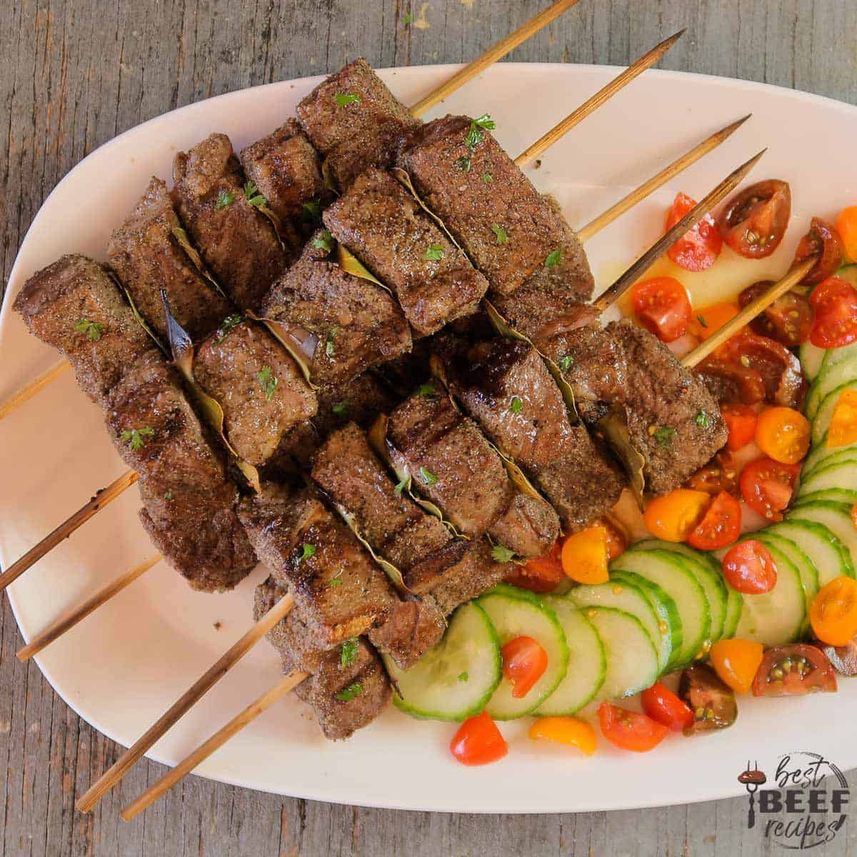 Beef kabobs with a tomato cucumber salad on a white platter