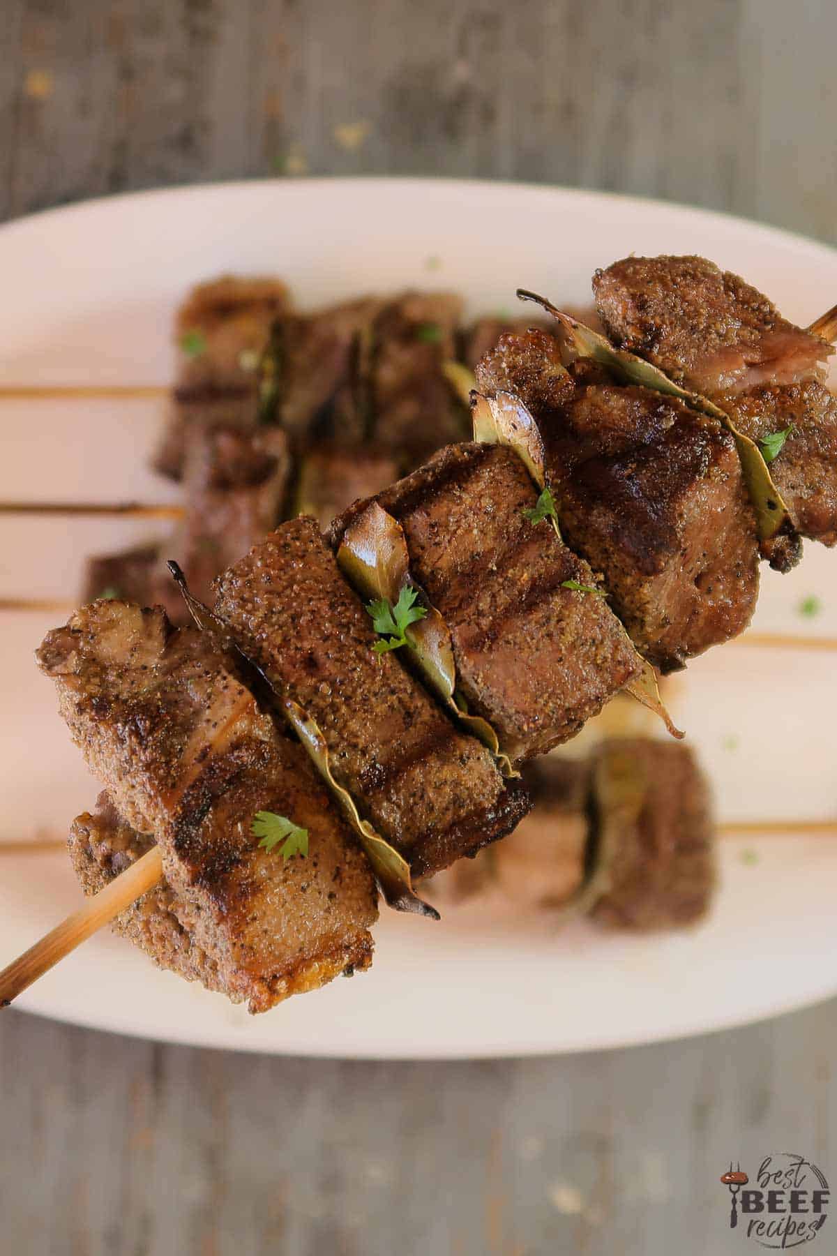 Holding up a beef kabob over a plate of kabobs