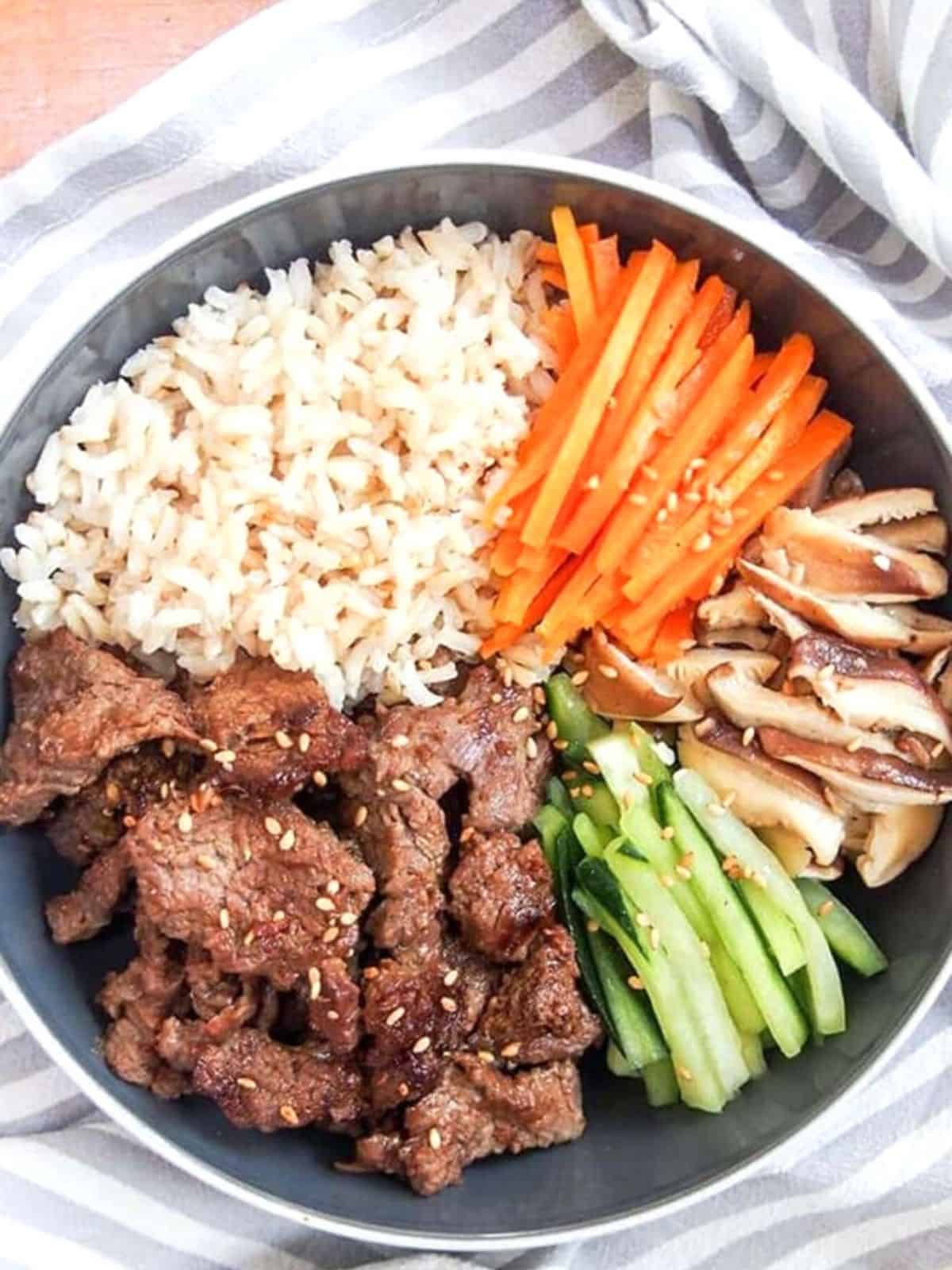 Fried beef over rice with cut vegetables in a bowl.