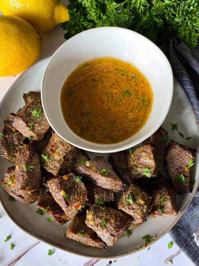 Air fryer steak bites on a plate with a bowl of cowboy butter