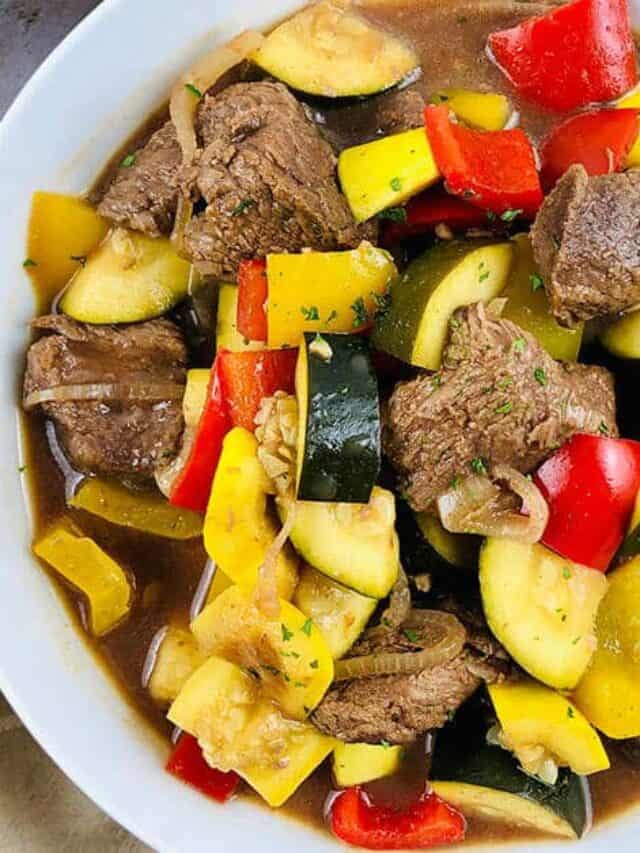 Beef stew in a bowl with bright vegetables.