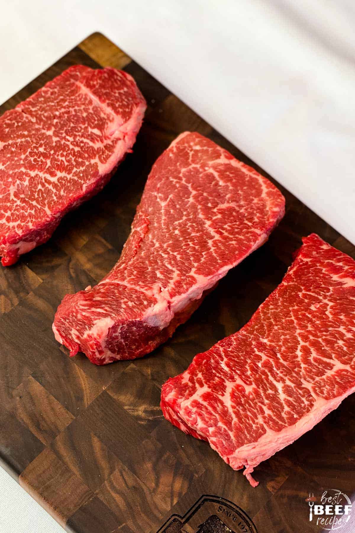 Three beautifully marbled beef short ribs on a cutting board