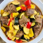 Beef stew in a bowl with bright vegetables.