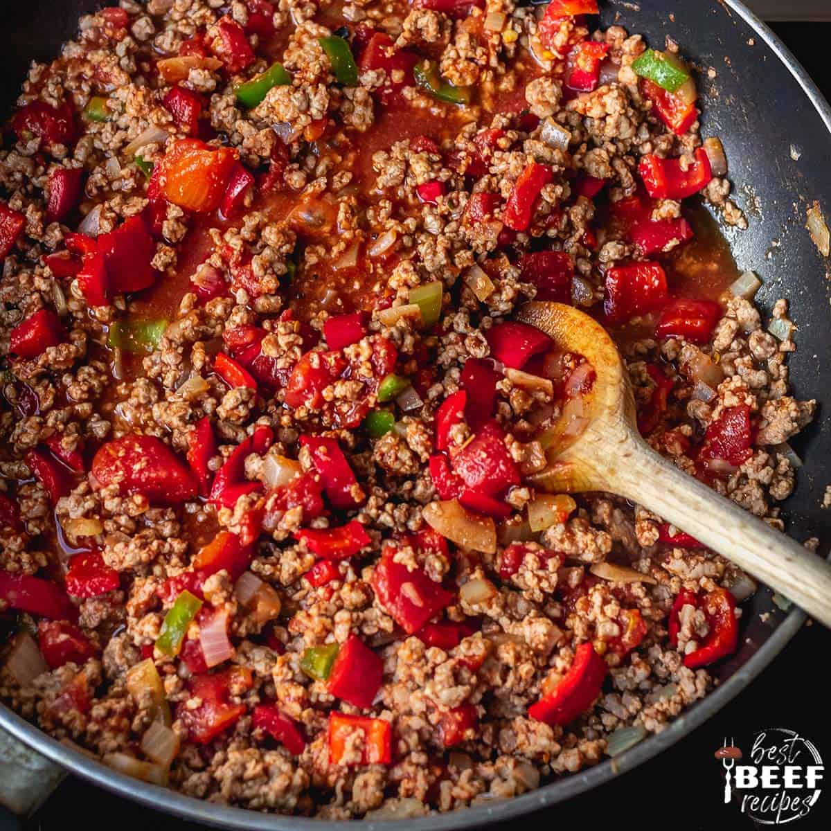 Ground beef cooking in a skillet with seasonings and peppers