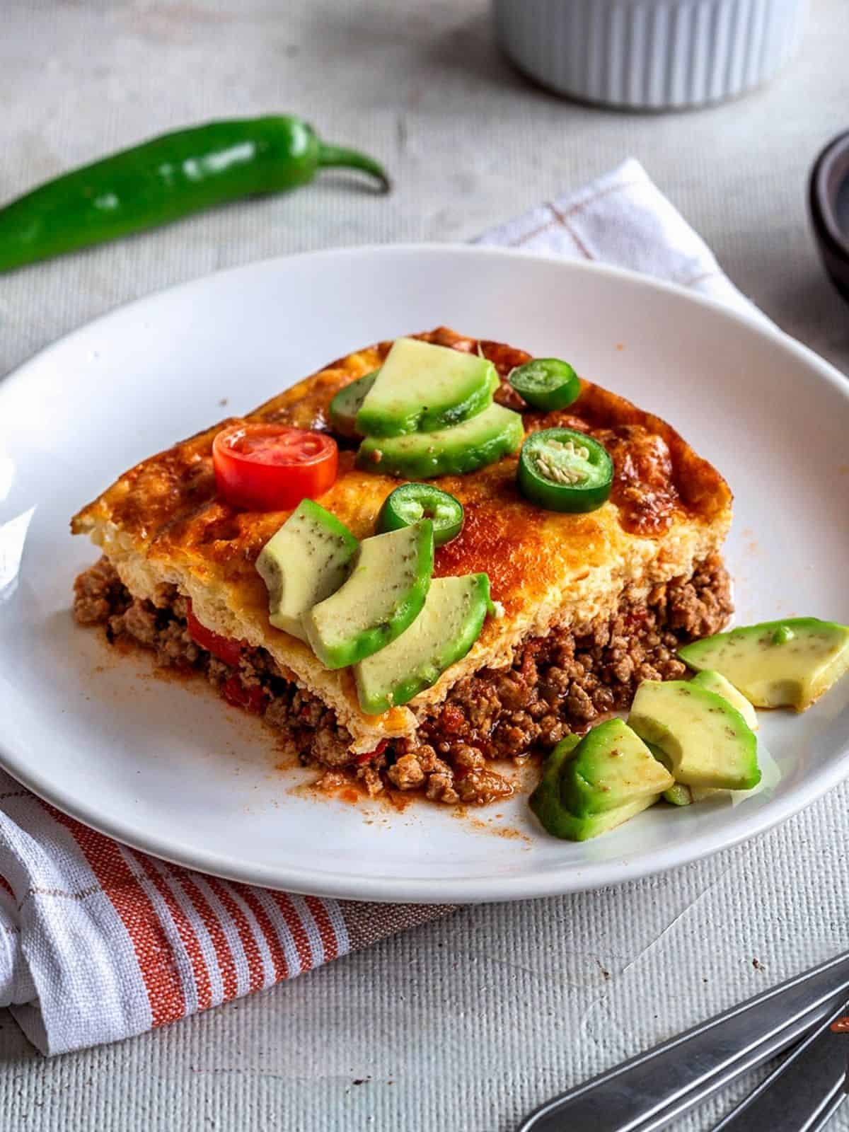 Slice of taco casserole topped with avocado and jalapeños