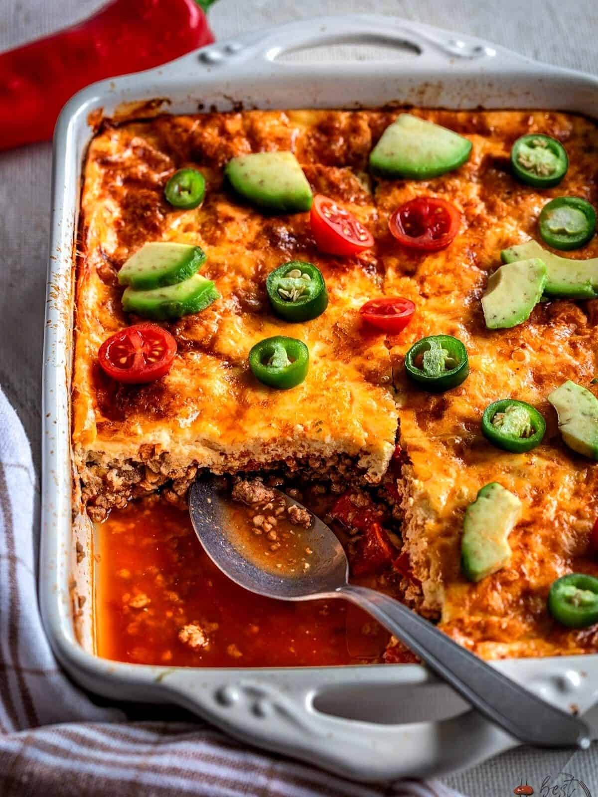 Taco casserole in a baking dish with one portion taken out.