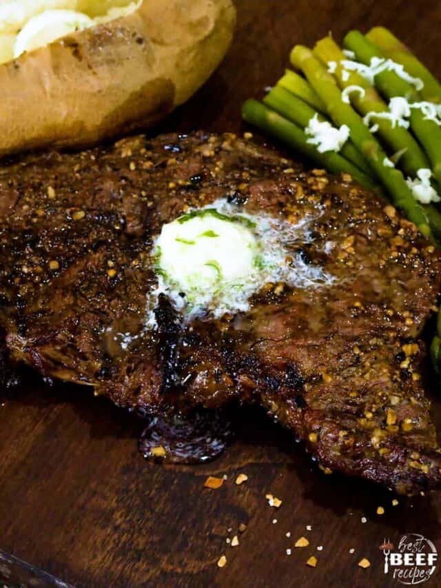 Grilled rib eye steak with garlic butter on top and asparagus to the side with a baked potato