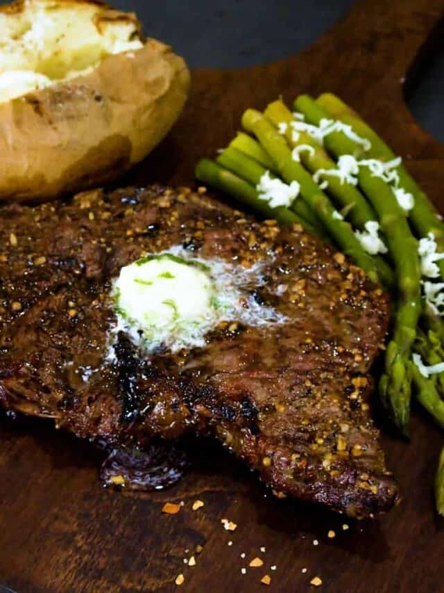 Grilled rib eye steak on a cutting board with asparagus and a baked potato