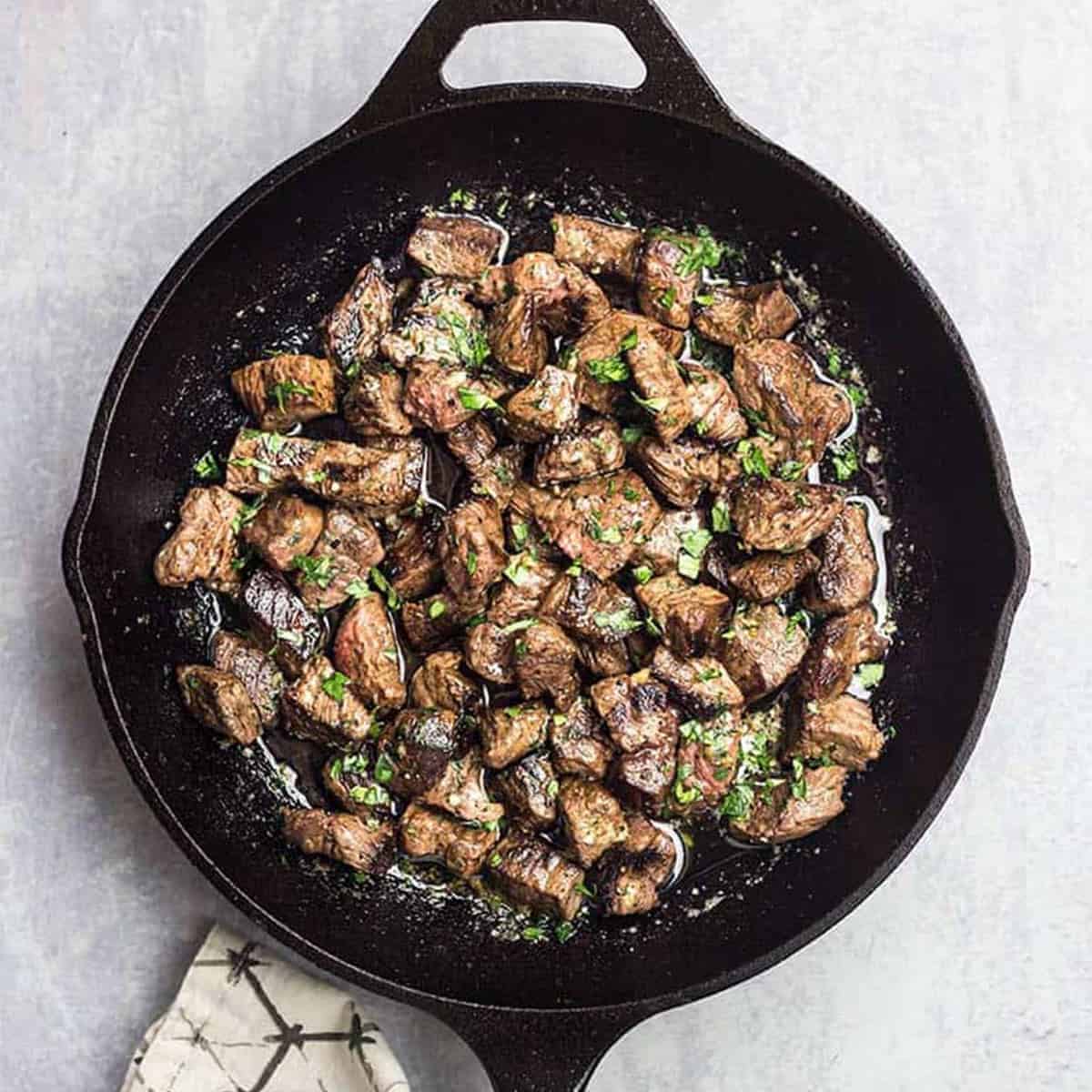 Steak bites in a cast iron skillet covered with garlic butter