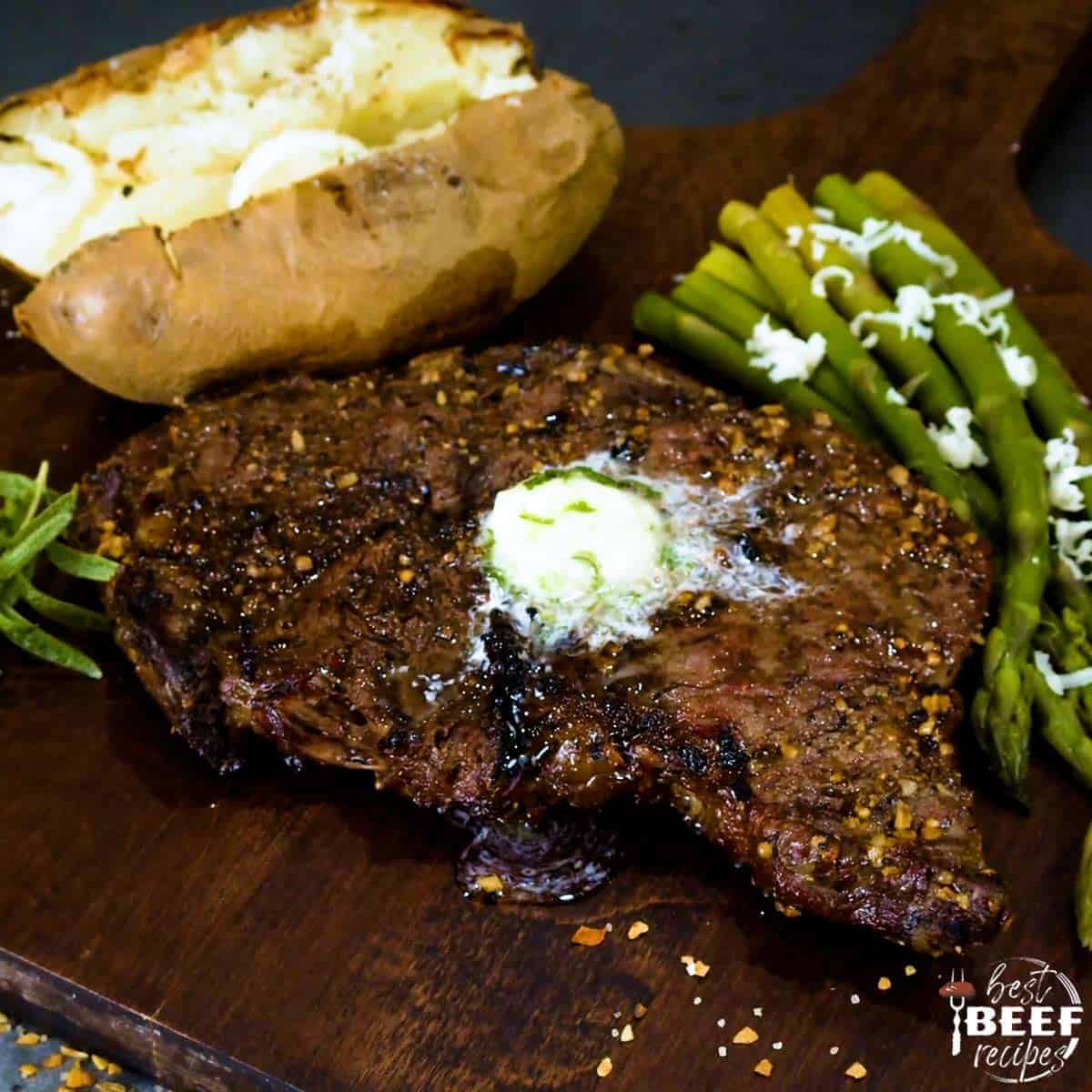 Grilled rib eye steak on a cutting board with asparagus and a baked potato