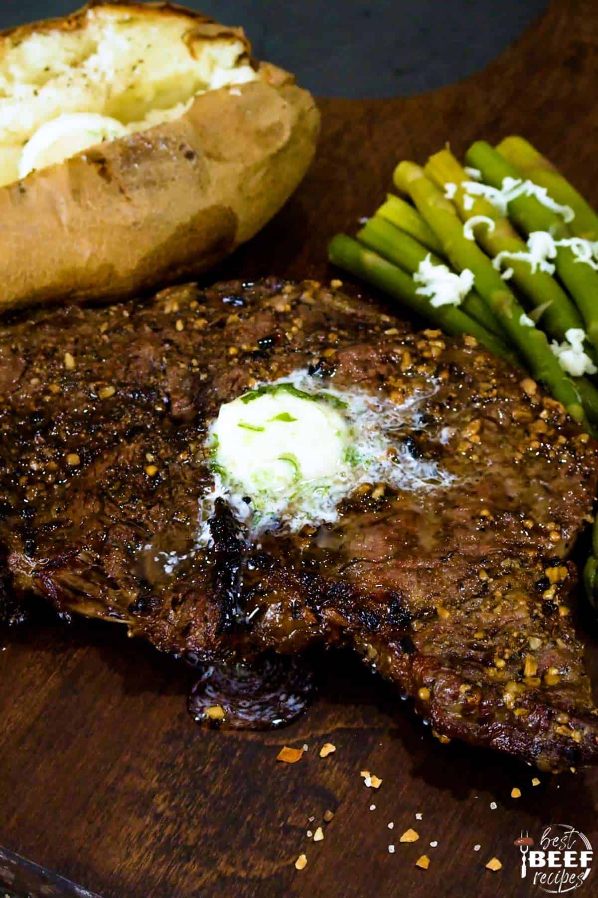 Grilled rib eye steak with garlic butter on top and asparagus to the side with a baked potato