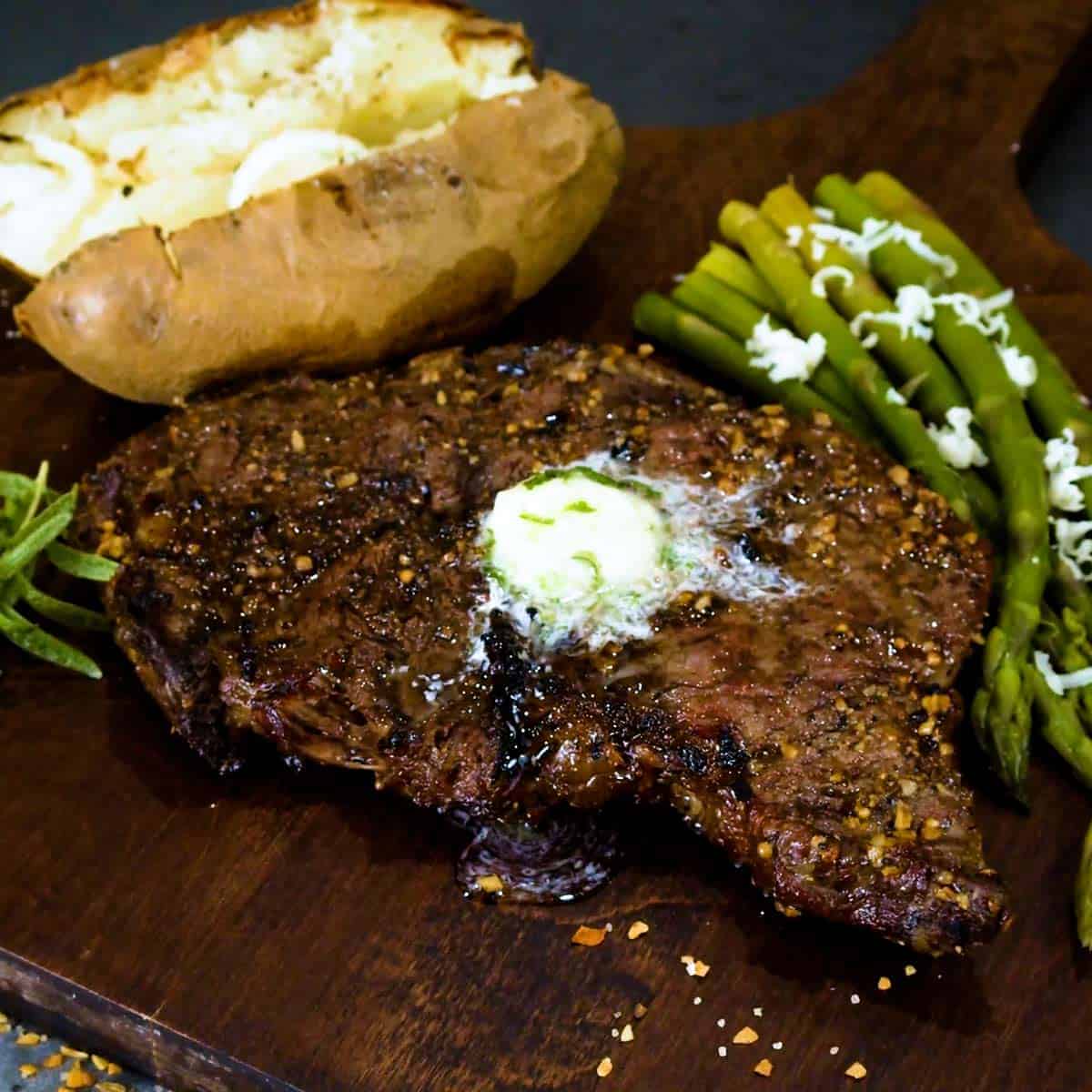 Grilled rib eye steak on a cutting board with asparagus and a baked potato