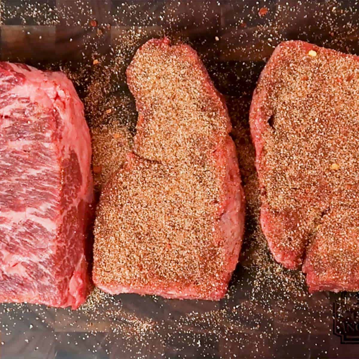 Three seasoned steaks on a cutting board