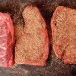Three seasoned steaks on a cutting board