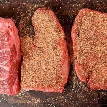 Three seasoned steaks on a cutting board