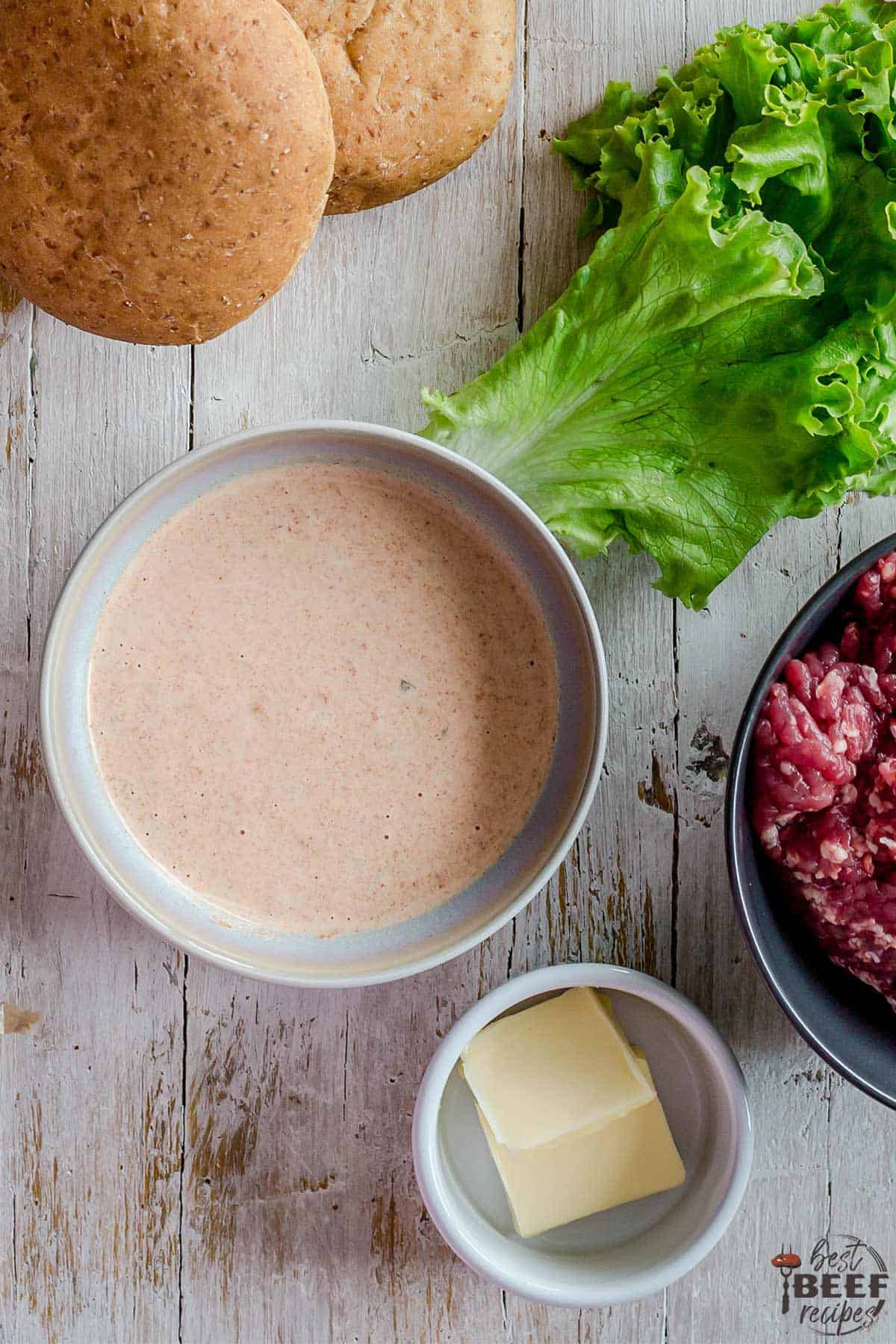 special burger sauce in a bowl near butter, lettuce, beef, and buns