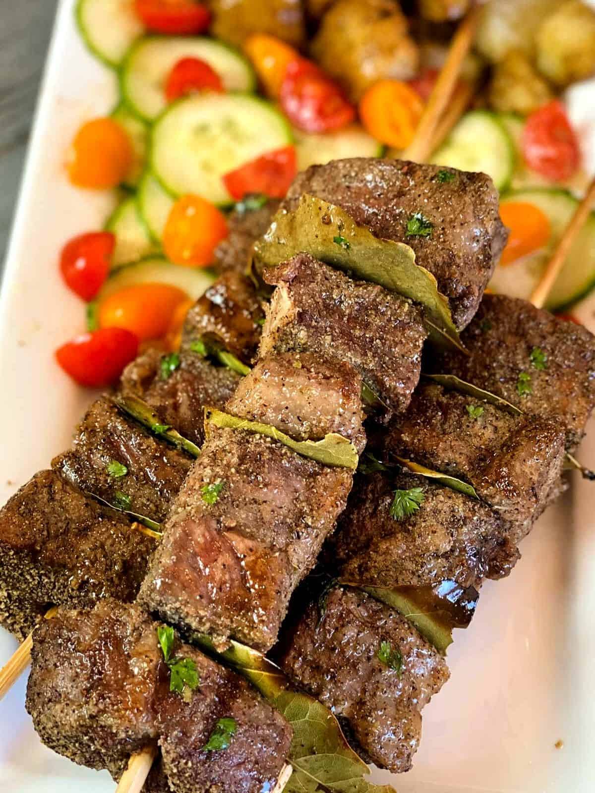 Beef kabobs with bay leaves in between, served with veggies.