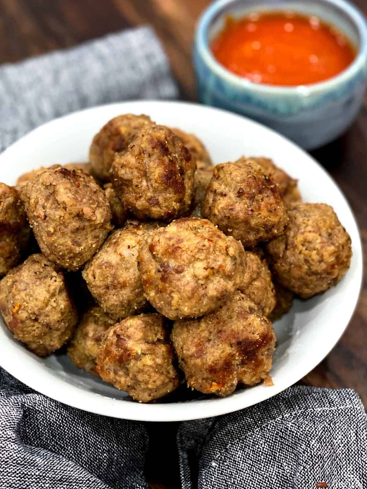 Meatballs in a bowl with red sauce in the background.