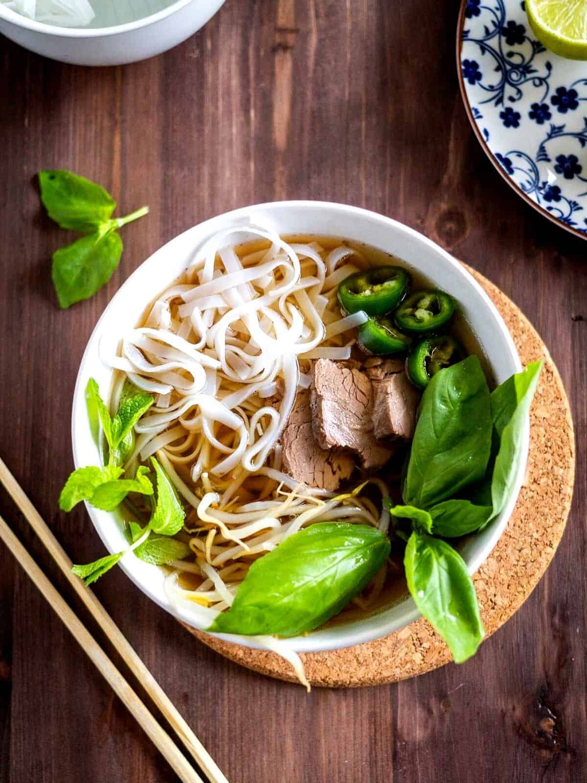 Beef Pho served with broth, noodles and basil in a bowl.