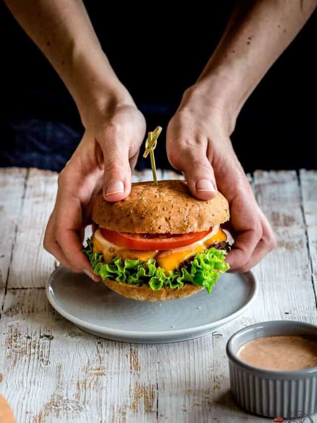 Burger being held by two hands above a plate.