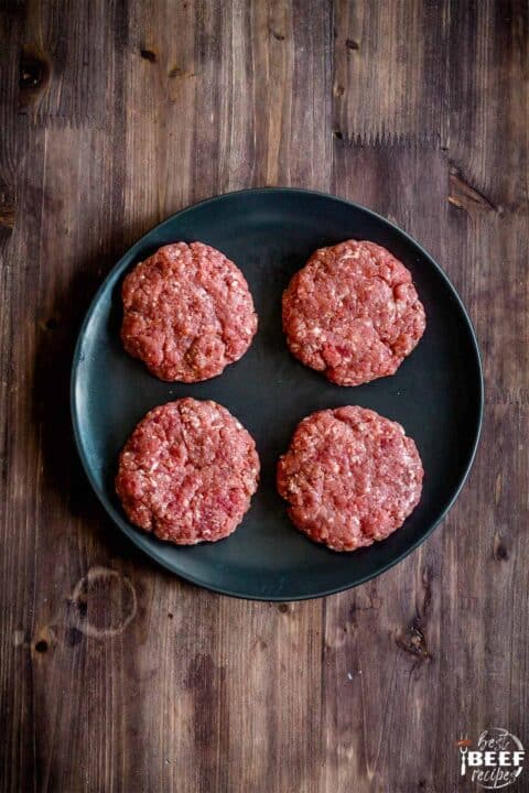 Four burger patties on a black plate