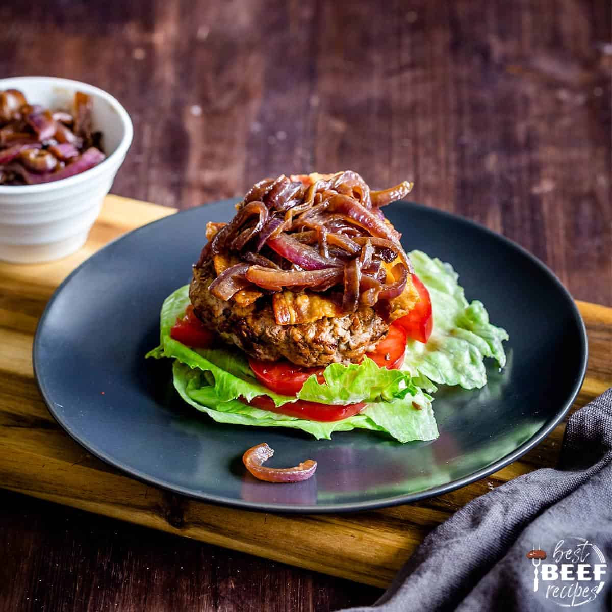 Keto burgers topped with caramelized onions on a bed of tomatoes and lettuce