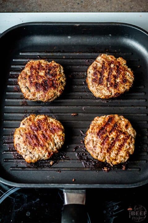 four burger patties on a grill pan after flipping
