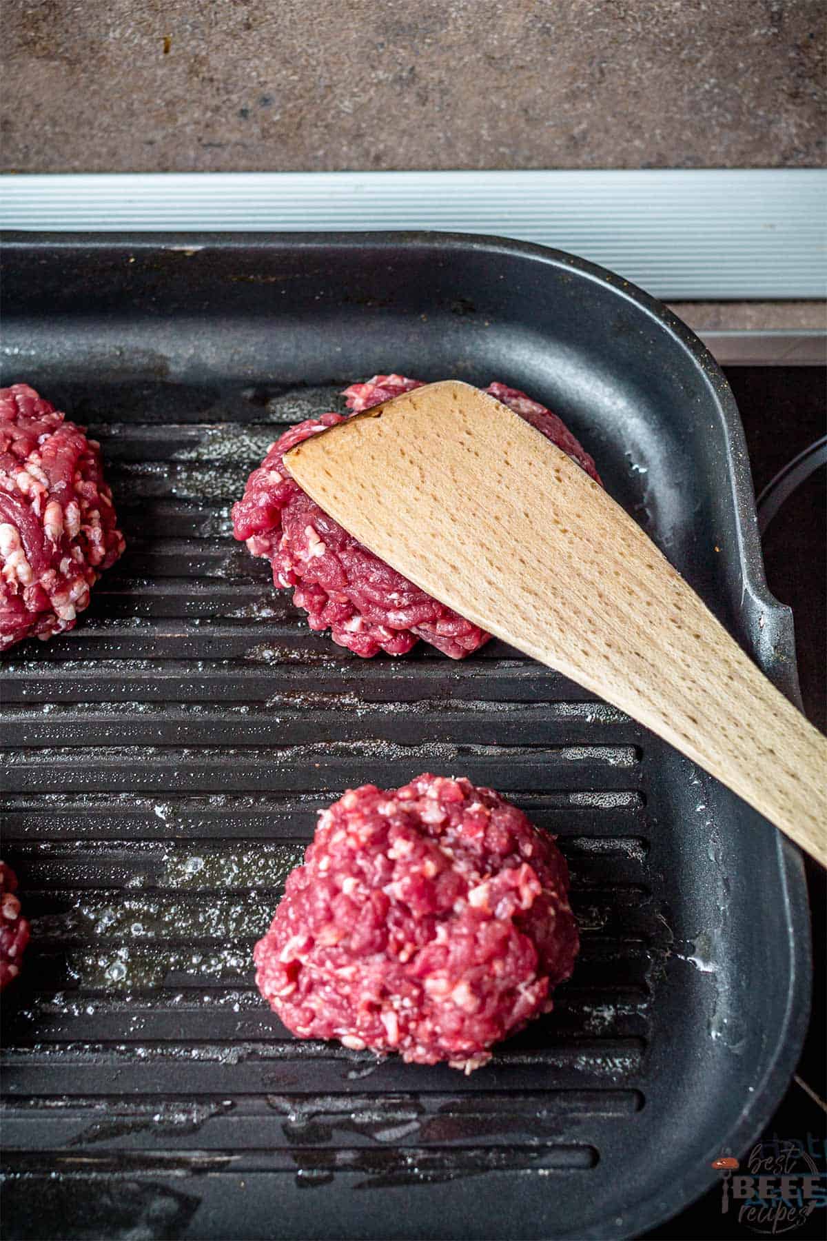Smashing burgers on griddle pan with a spatula