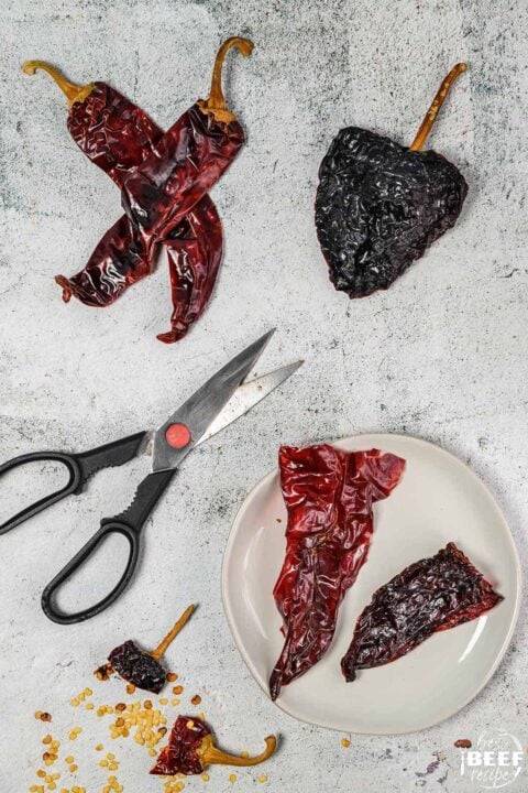 Guajillo and ancho chiles on a surface with scissors and a bowl