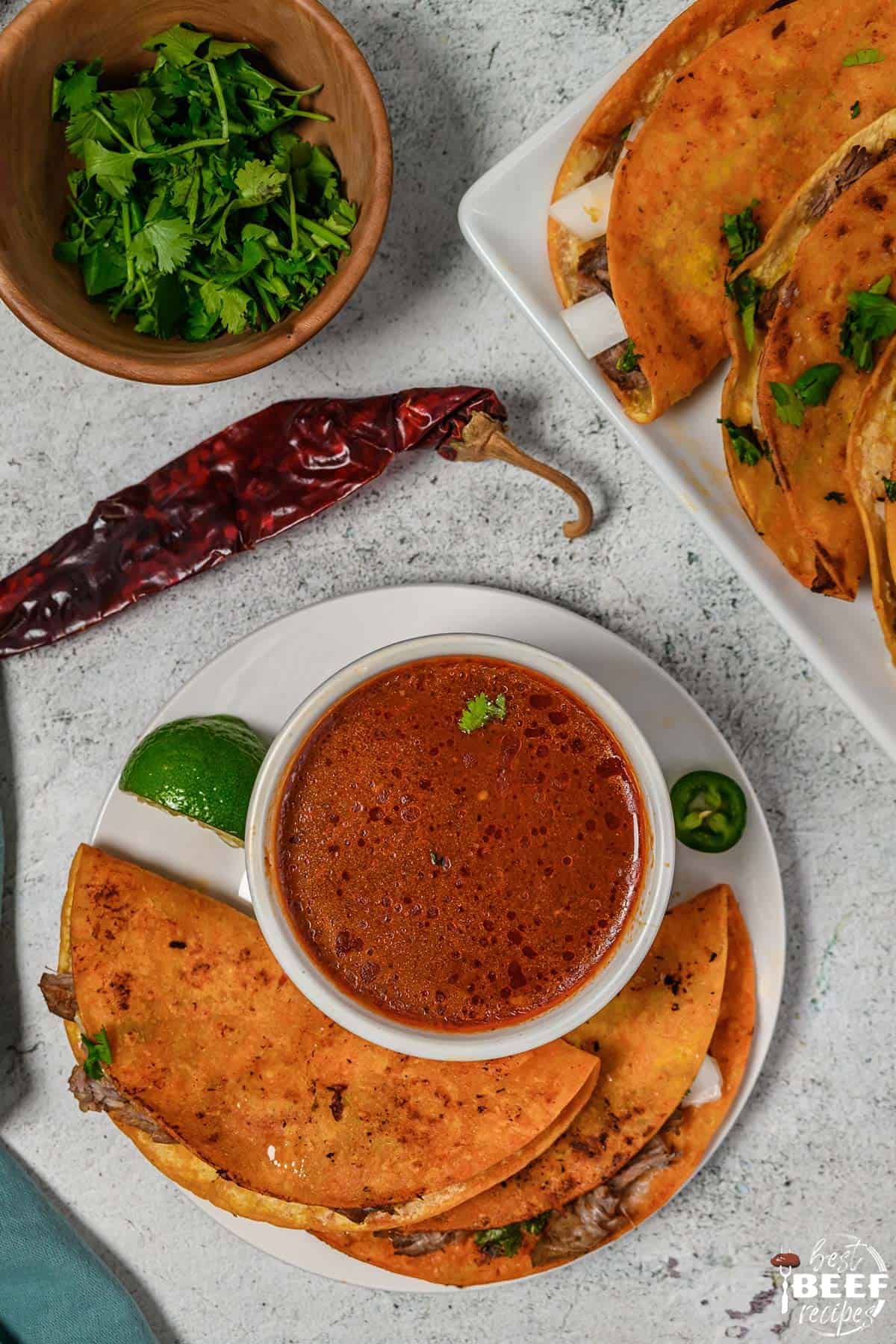 Birria tacos on a plate with stew in a bowl