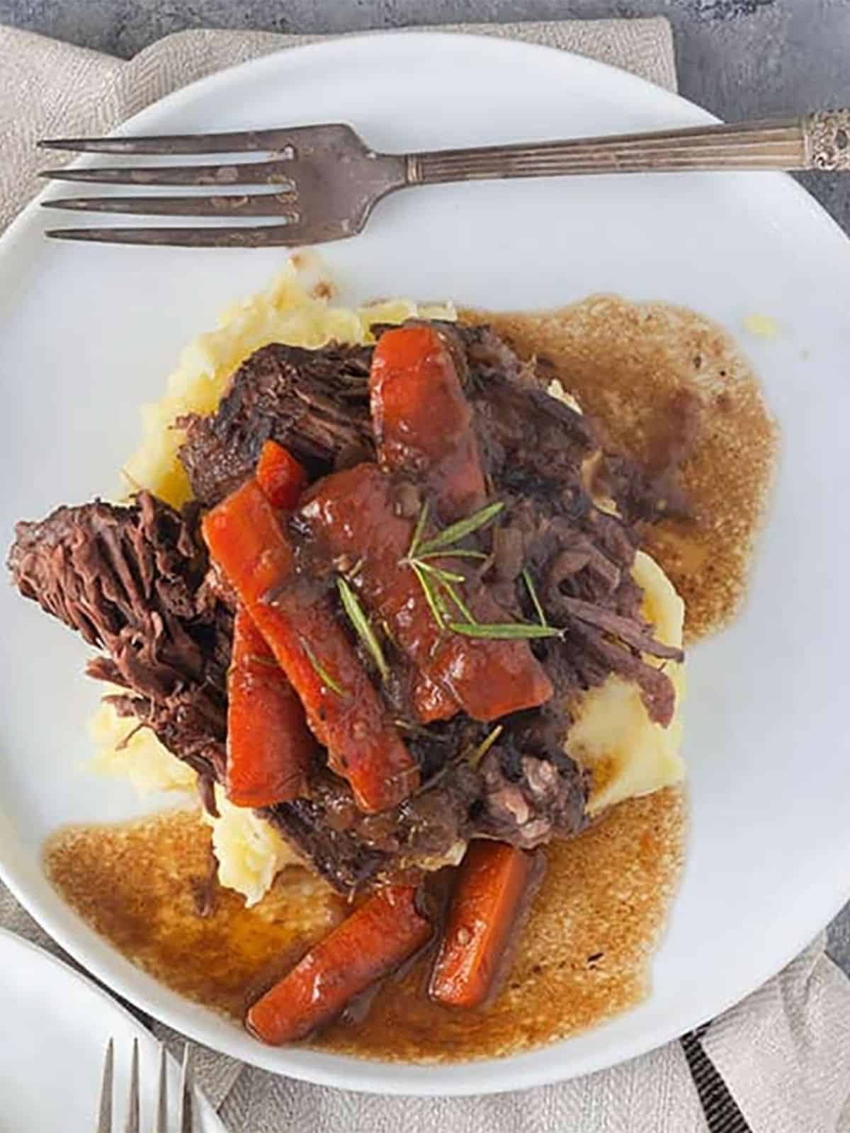 Pot roast over mashed potatoes with gravy and carrots.