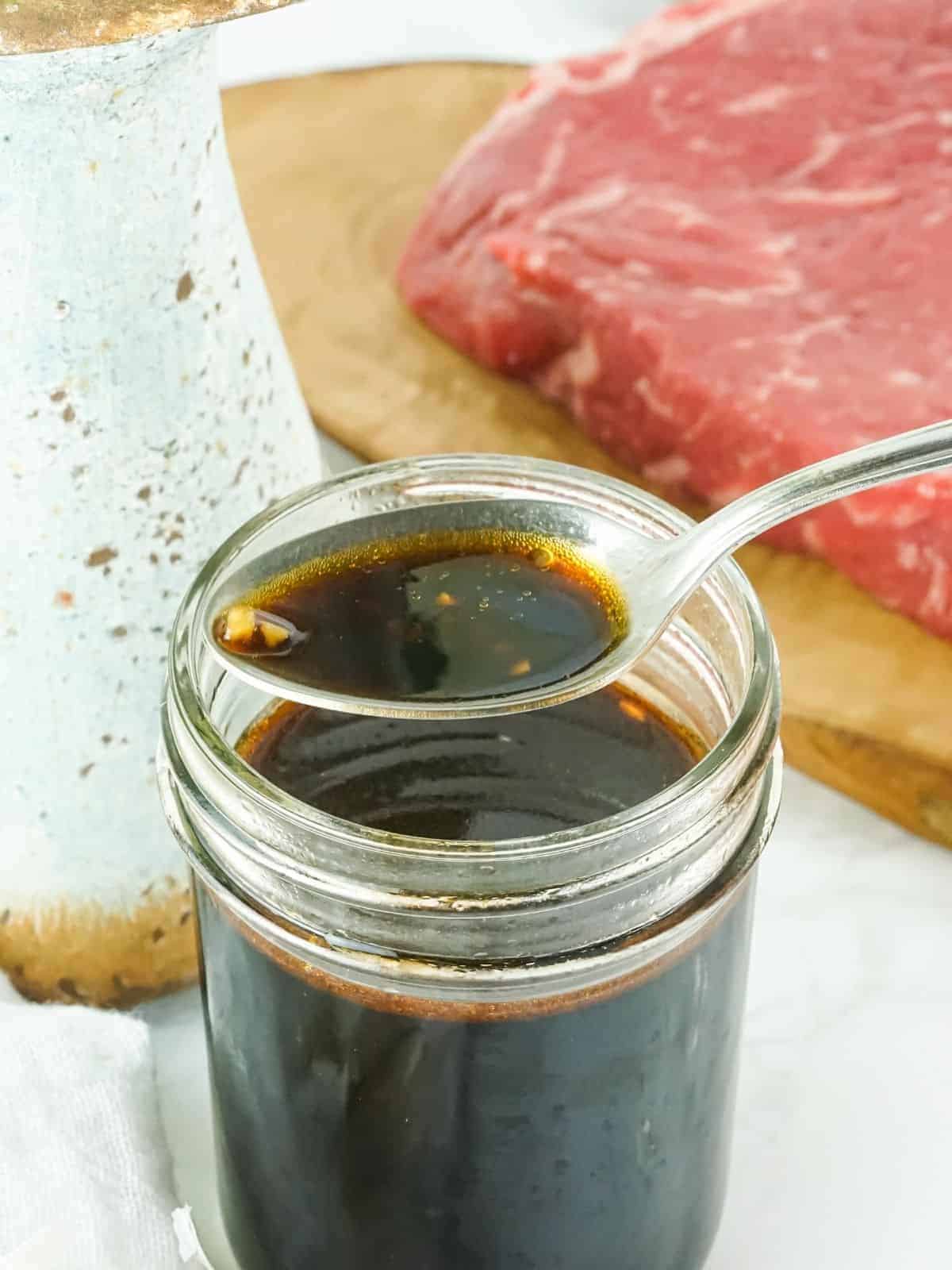 Dark marinade in a glass jar with a silver spoon.