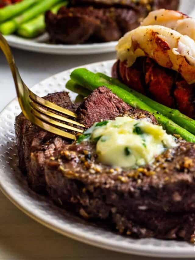 Steak topped with garlic butter served with asparagus and lobster.