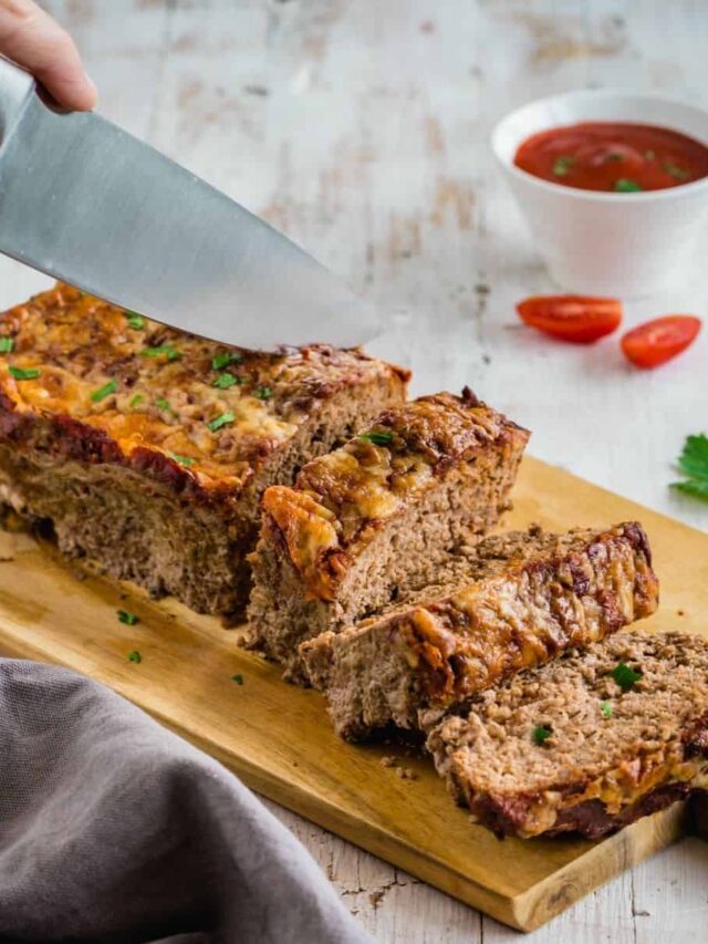 Cheesy meatloaf on a cutting board with 2 slices and being sliced.