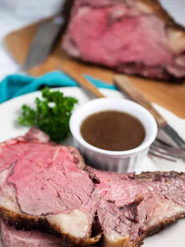 Boneless prime rib in slices on a plate with sauce on the side.