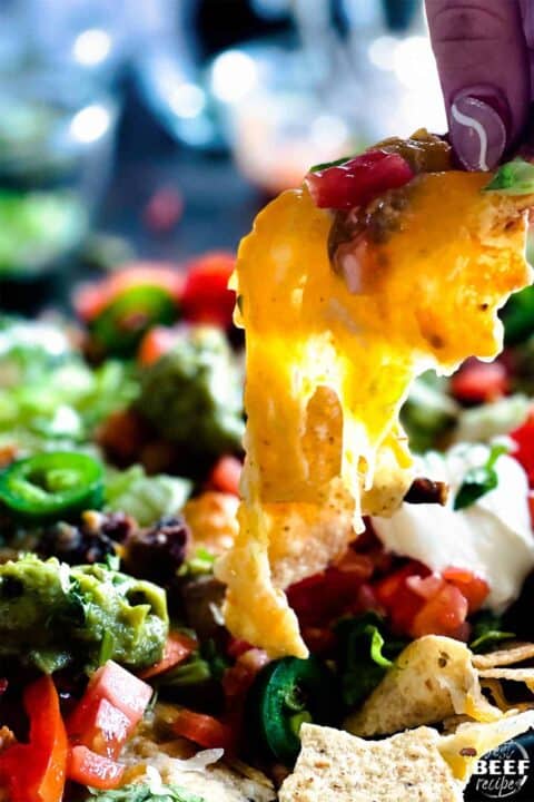 Pulling a nacho out of the sheet pan with ooey gooey cheese