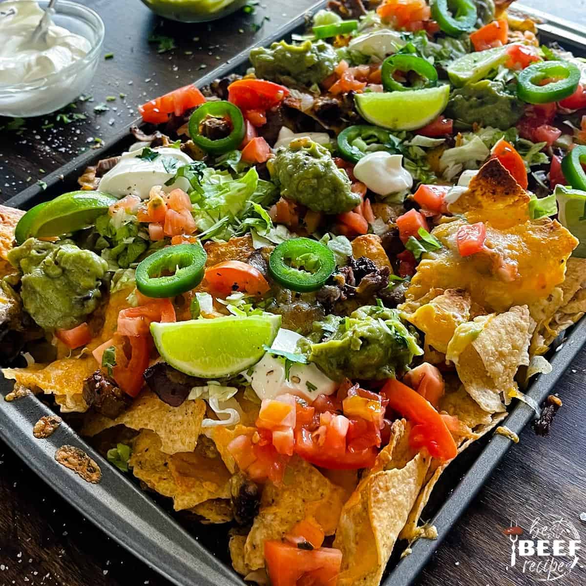 steak nachos on a tray with limes and guacamole