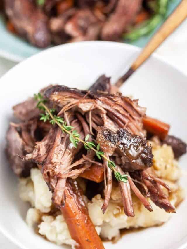 Pot roast with veggies served over mashed potatoes in a bowl.