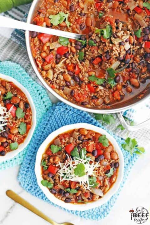 A pot of ground beef chili with two bowls of chili