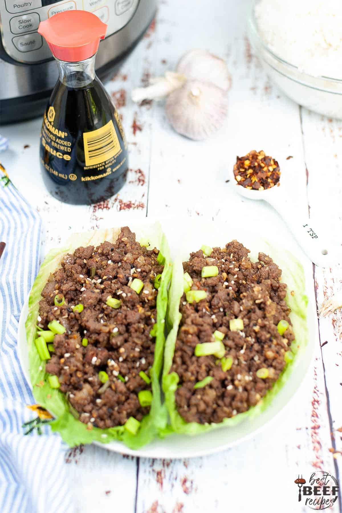 Korean ground beef in two lettuce cups near a bottle of soy sauce
