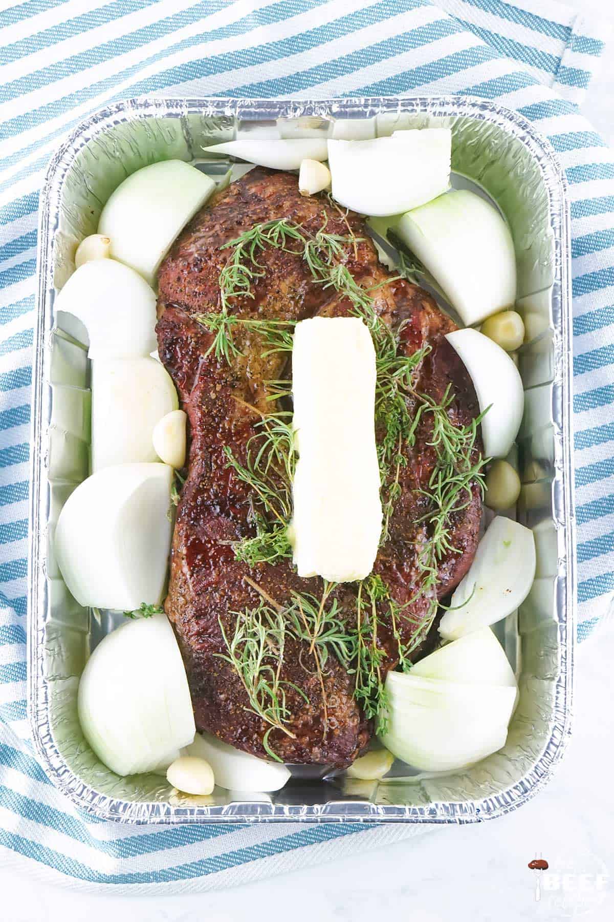 Chuck roast in a roasting pan with butter, onions and herbs