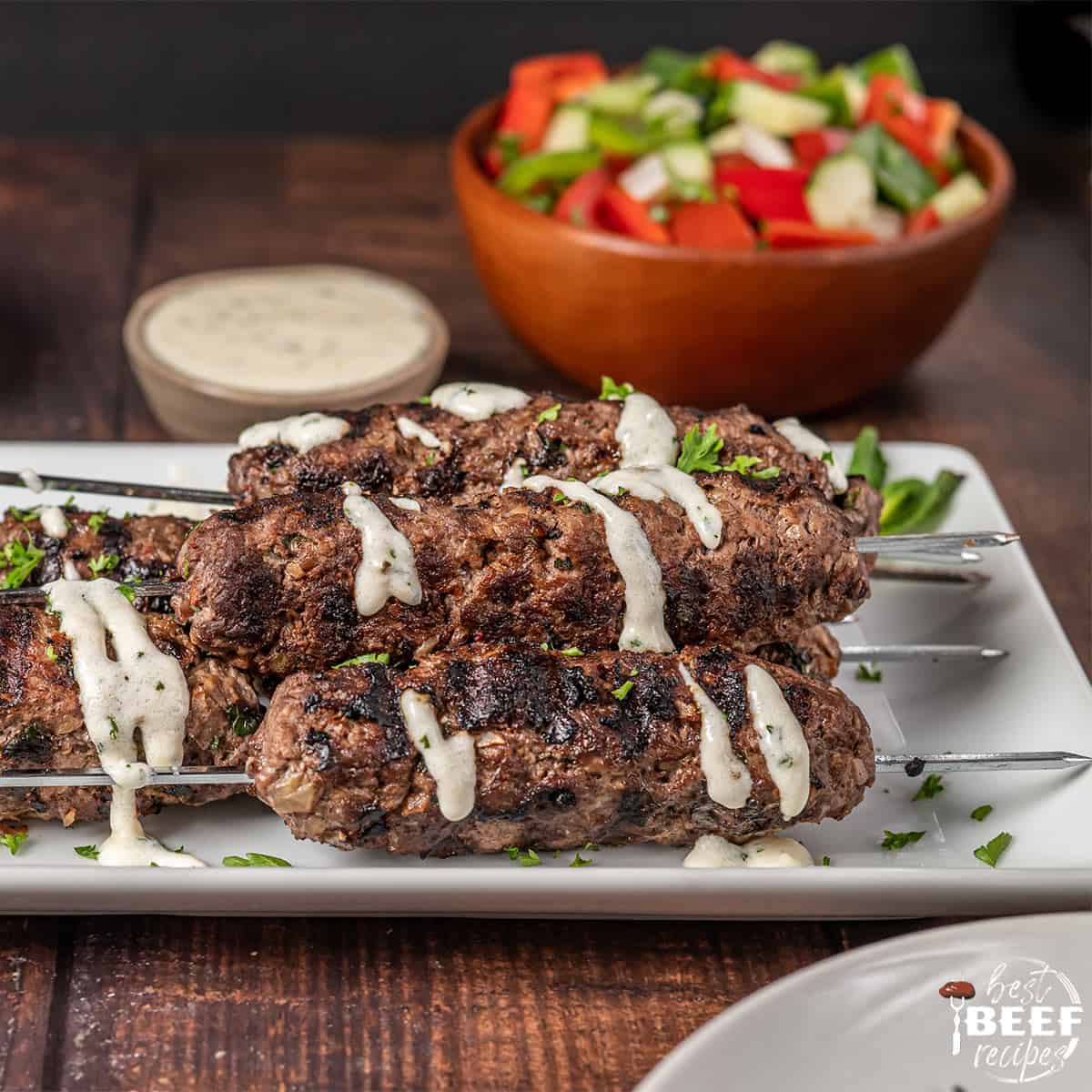 Kofta kebabs on a white platter with garlic sauce