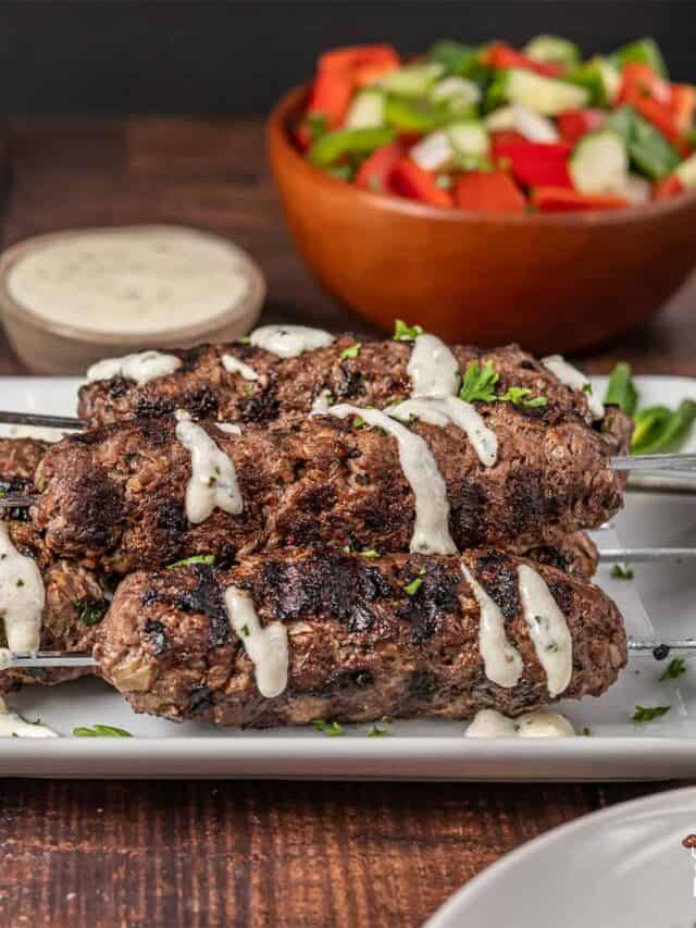 Kofta kebabs on a white platter with garlic sauce
