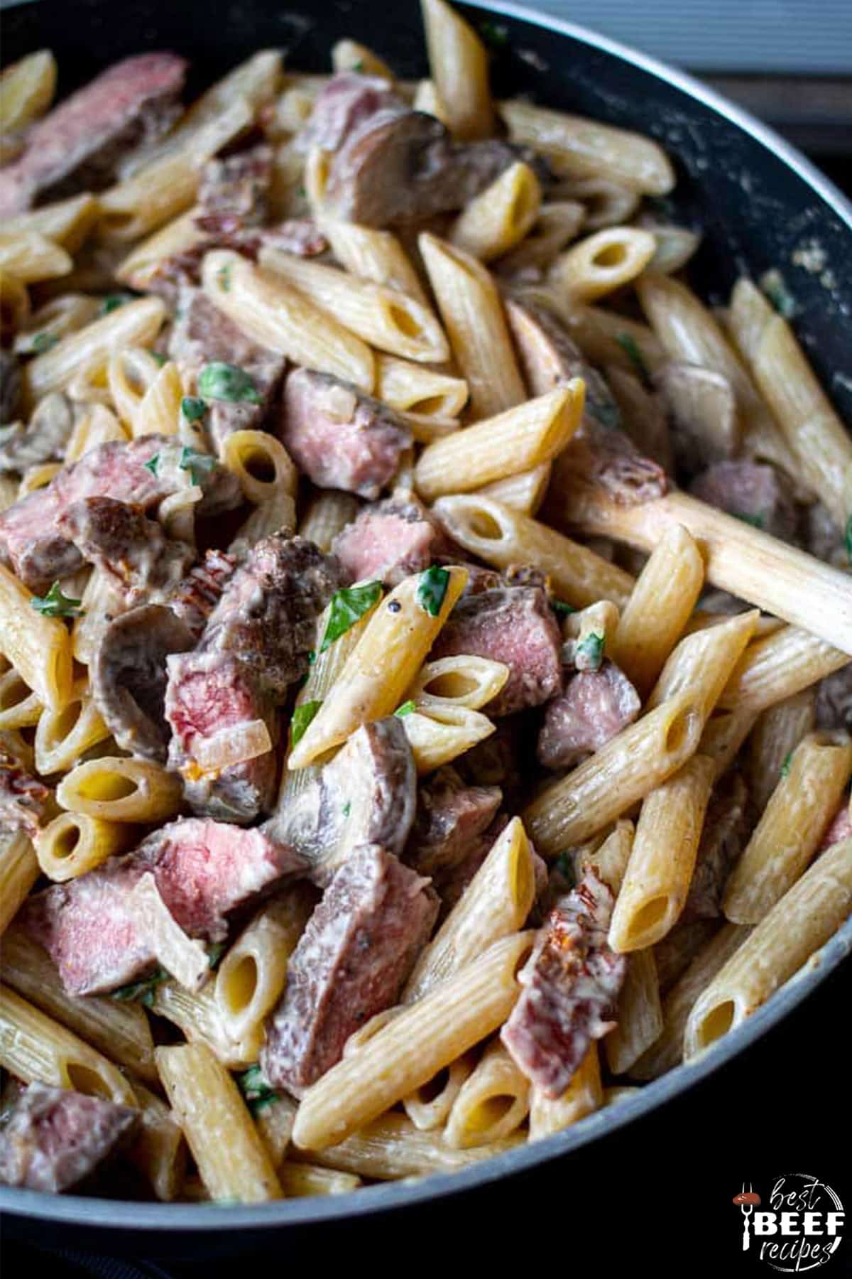 creamy leftover prime rib pasta in a skillet with a wooden spoon
