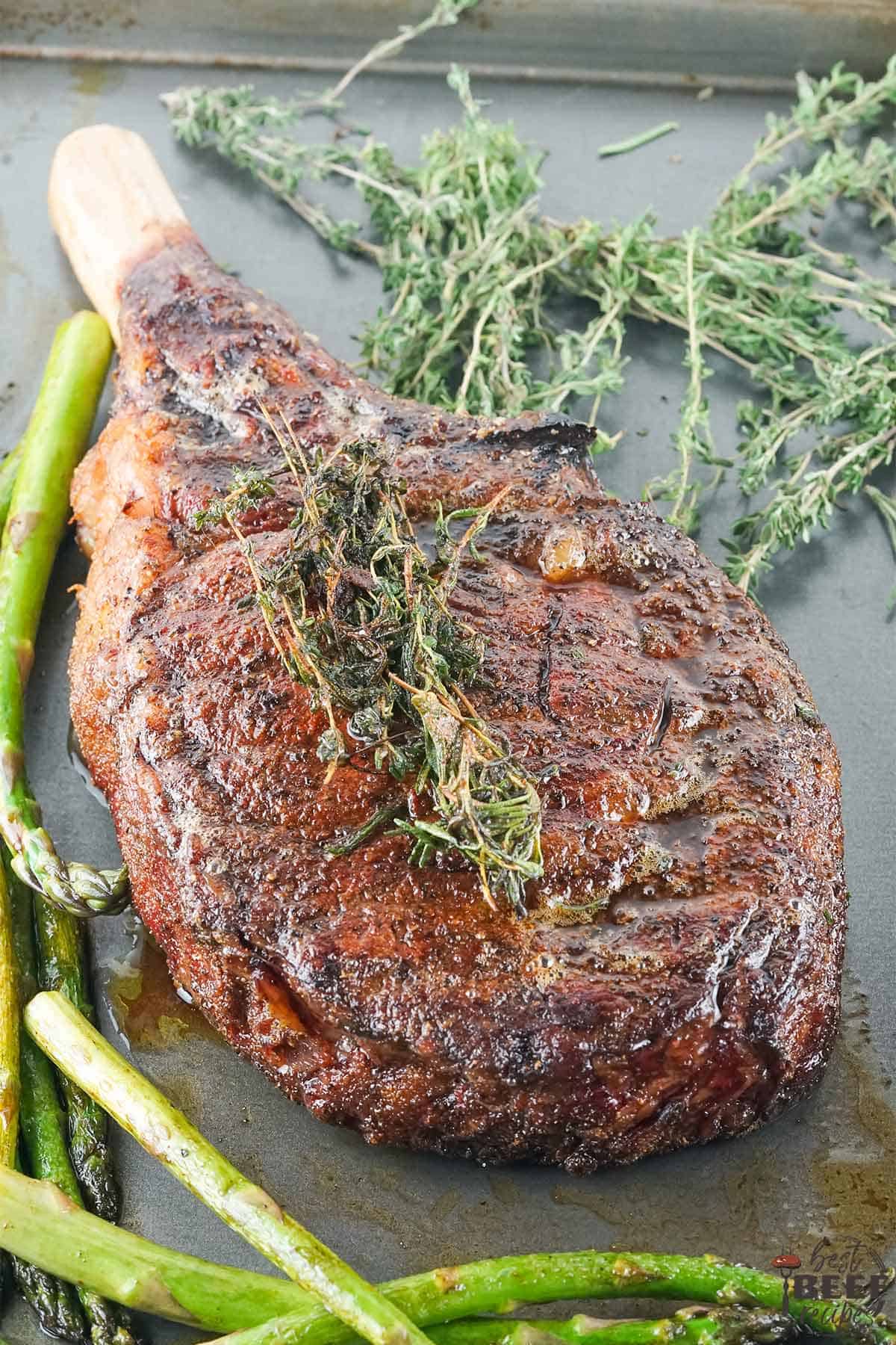 Tomahawk steak on a tray with thyme and asparagus