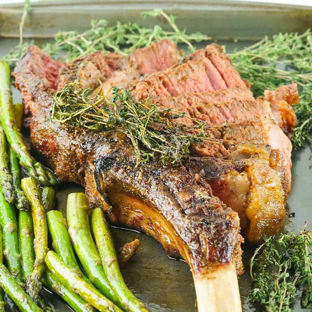 Tomahawk steak sliced on one side with asparagus and herbs