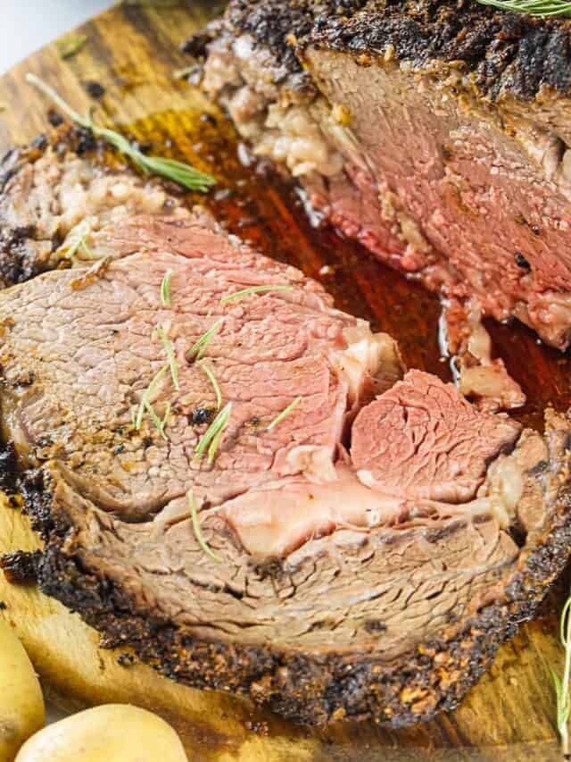 Sliced prime rib on a cutting board with potatoes and herbs